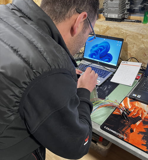 Un technicien en veste noire analyse la reprogrammation sur un ordinateur portable dans un atelier.
