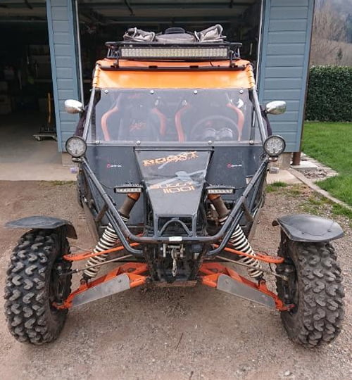 Un véhicule tout terrain noir et orange, optimisé après une reprogrammation moteur, stationné devant un garage.